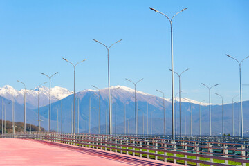 Outdoor tables with lanterns on a landscaped city street, in the background a mountain landscape with forests on the slopes and snow and glaciers on the peaks.