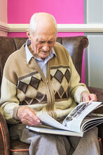 Senior Man Sitting In A Chair Looking At A Book About World War 2; Hartlepool, County Durham, England