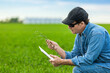 © Designpics - Farmer holding a seedling in his hand while using a tablet with a farm field and crop in the background; Alberta, Canada