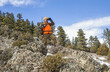 © Designpics - Hunter with orange vest and rifle standing on a hillside and looking out with binoculars; Denver, Colorado, United States of America