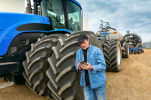 Farmer Using A Smart Phone While Standing On A Farm Beside Equipment; Alberta, Canada