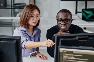 Multiethnic couple of developers working on computer together to develop new program