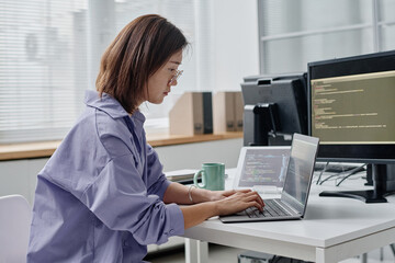 Asian young woman writing codes on laptop while working at her workplace in office