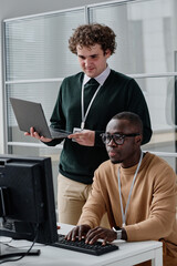 african american developer typing codes on keyboard with his colleague standing in background and ch