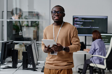 portrait of african american it specialist in eyeglasses smiling at camera while working online on d