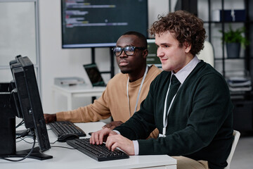 Two IT specialists working together with computer codes for new software on computer during teamwork in office