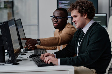 programmer pointing at computer monitor with codes and talking to his colleague while they working w