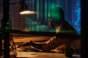 African American programmer concentrating on his work on computer he working overtime in dark office