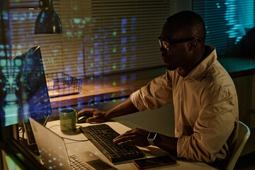African American businessman typing keyboard security codes on computer while working overtime in office
