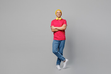 Wall Mural - Full body cheerful fun smiling young man of African American ethnicity 20s he wears pink t-shirt yellow hat headphones hold hands crossed folded look camera isolated on plain grey background studio.