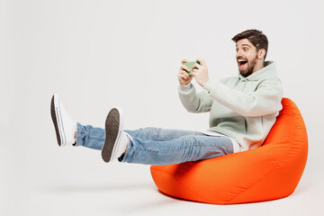 Wall Mural - Full body young gambling man in mint hoody sit in bag chair use play racing app on mobile cell phone hold gadget smartphone for pc video games isolated on plain solid white background studio portrait.