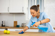 Attentive woman uses spray while wiping the tabletop with a rag in a modern kitchen at home