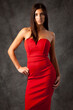 © Designpics - Portrait of young woman in red dress, standing and posing with hand on hip, looking at camera, grey background