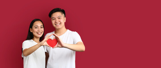 Wall Mural - Happy young Asian couple holding paper heart on red background with space for text. Valentine's Day celebration