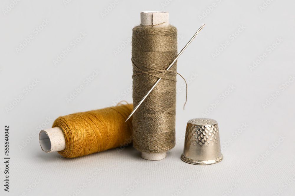 Thread spools with needle and thimble on grey background