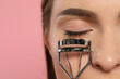 Woman with eyelash curler on pink background, closeup. Space for text