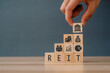 Businessman hand arranging wood block with REIT. Cube wooden block with alphabet building the word REIT on blackboard. Real estate investment trust concept.