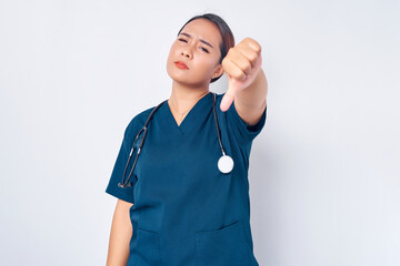 Wall Mural - Upset young Asian woman nurse wearing blue uniform with a stethoscope showing thumbs down and expressing disappointment isolated on white background. Healthcare medicine concept