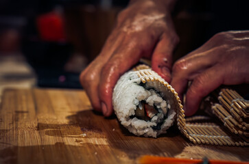 Wall Mural - Japanese chef making California Maki Sushi with Masago - Roll made of Crab Meat, Avocado, Cucumber inside. Masago (smelt roe) outside with tuna, salmon, shrimp,traditional Japanese food ,Dark Tone