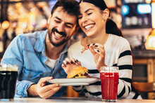 Young Couple In Love Having Fun Spending Leisure Time Together At Restaurant, Eating Burgers And Drinking Beer