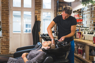 Pregnant woman at hairdresser salon. Male hair stylist washing long hair of his customer in a modern industrial hair salon. High quality photo