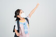 Asian little child girl carry a backpack wearing respirator mask to protect coronavirus outbreak and pointing hand to blank background, New virus Covid-19