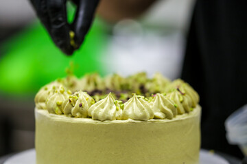 cake chef designer sprinkling the top of green layered frosted chocolate cake at kitchen lab with pistacchio and dark chocolate