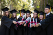 © Михаил Решетников - Row of happy young people in graduation gowns holding diplomas outdoors.