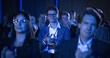 © Gorodenkoff - Crowd of Smart Tech People Applauding in a Dark Conference Hall During a Motivational Keynote Presentation. Business Technology Summit Auditorium Room Full of Delegates. Male in Focus.