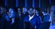 © Gorodenkoff - African Male Sitting in a Dark Crowded Auditorium at a Tech Conference. Professional Using a Laptop Computer. Specialist Watching Innovative Technology Presentation About New Software Solutions.