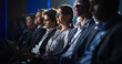 © Gorodenkoff - Female Sitting in a Dark Crowded Auditorium at a Tech Conference. Young Woman Using Laptop Computer. Specialist Watching Innovative Technology Presentation About New Software and High Tech Products.
