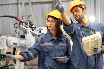 Male industrial engineer using remote control board to check robotic welder operation in modern automation factory. Woman technician monitoring robot controller system for automated steel welding.