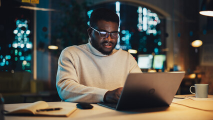 Poster - Slightly Agitated Male Employee Working on Laptop Computer in Office During Evening Time. Diverse Black African Specialist Browsing Internet, Researching Financial Data, Answering to a Work Email.
