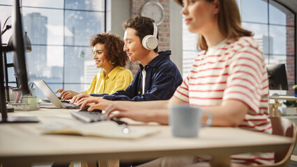 Poster - Group of Multiethnic Young Creative Colleagues Sitting Next to Each other and Working On Computers in Modern Office. Biracial Woman and Asian man Smiling After Successfully Finishing Tasks.