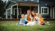 Portrait Of A Happy Young Family Couple With A Son And Daughter, And A Noble White Golden Retriever Dog Sitting On A Grass In Their Front Yard At Home. Cheerful People Looking At Camera And Smiling.