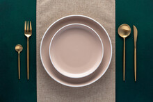 Festive Place Setting With Beige Napkin. Empty Plates And Gold Cutlery On Dark Green Background. Top View. Dining Table In Luxury Restaurant. Card Or Menu Template, Flat Design. Tableware, Crockery.