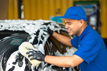 Wall Mural - Man worker washing car service with foam and sponge. Car wash cleaning wipe station. Employees clean a vehicle professionally.