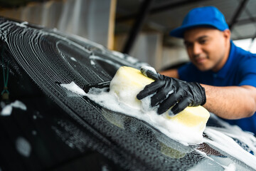 Wall Mural - Man worker washing car service with foam and sponge. Car wash cleaning wipe station. Employees clean a vehicle professionally.