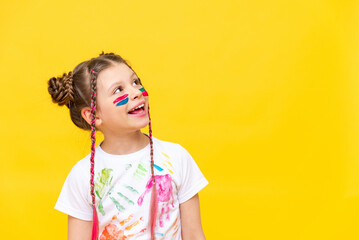 Wall Mural - A little girl, painted with paints, looks at your advertisement on a yellow isolated background. The art of painting with paints for children. Art courses for schoolchildren.  Copy space.