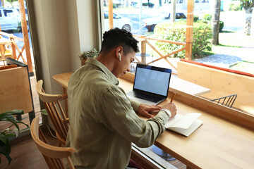 Hispanic young man sitting in coffee shop with his laptop and working. remote job concept. Close up, copy space, background.