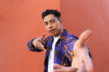 Wall Mural - Young man of hispanic heritage wearing colorful flannel shirt posing over orange wall. Copy space for text, close up, background.