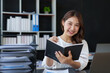© amnaj - Asian businesswoman secretary sitting happily working on laptop Take notes attentively and smile happily doing the assignments.