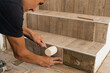 © ADDICTIVE STOCK - Crop man applying tile on stair