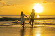 Playful romantic couple walking on sandy beach during the golden-hour sunset