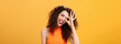 Carefree optimistic and energized good-looking woman with curly hairstyle tilting head and sticking out tongue playfully showing okay or excellent sign over eye posing near orange background