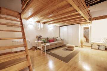 house with a mezzanine with a solid pine wood structure, beams and stairs and a three-seater sofa bed upholstered in beige fabric