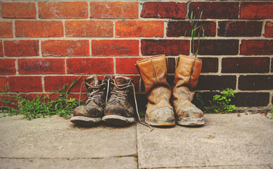 Wall Mural - Two pairs of old boots in front of a  brick wall.The boots are heavily worn steel toe cap safety boots.