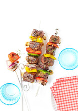 Grilled Beef And Vegetable Skewers With Turquoise Drinking Glasses And Red And White Checkered Napkins, Studio Shot On White Background
