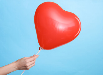 Wall Mural - Woman's hand holds red balloon in the shape of a heart on a blue background. Valentine's day concept