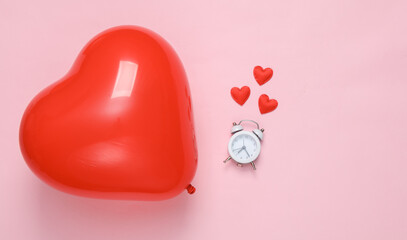 Red heart-shaped air balloon and alarm clock with many hearts on a pink background. Valentine's Day